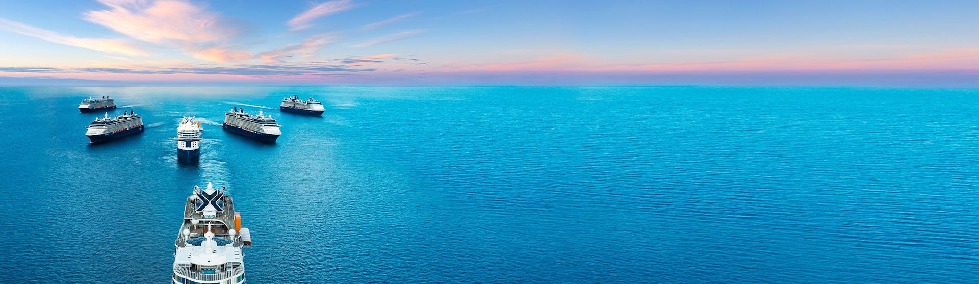 A fleet of cruise ships docked in crystal-clear turquoise waters under a vibrant sunset sky.